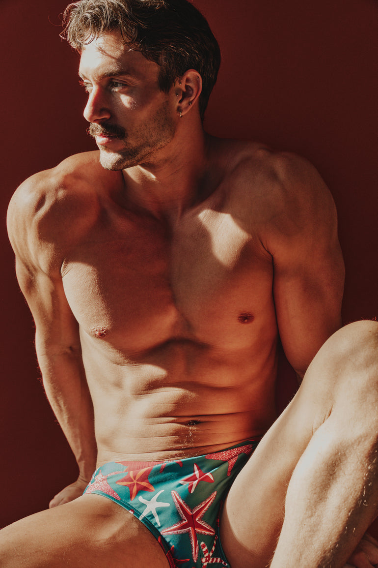 Man wearing colorful swim trunks with a starfish pattern against a red background